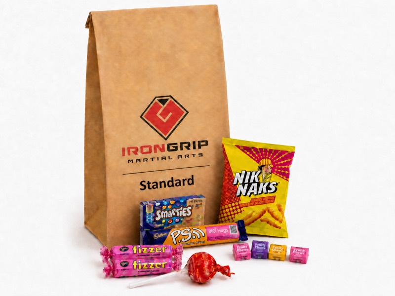 Standard Party Pack: a brown Iron Grip paper bag with a packet of Nik Naks, a box of Smarties, a Cadbury P.S. chocolate, two strawberry Fizzers, a lollipop and four Fruity Chews.